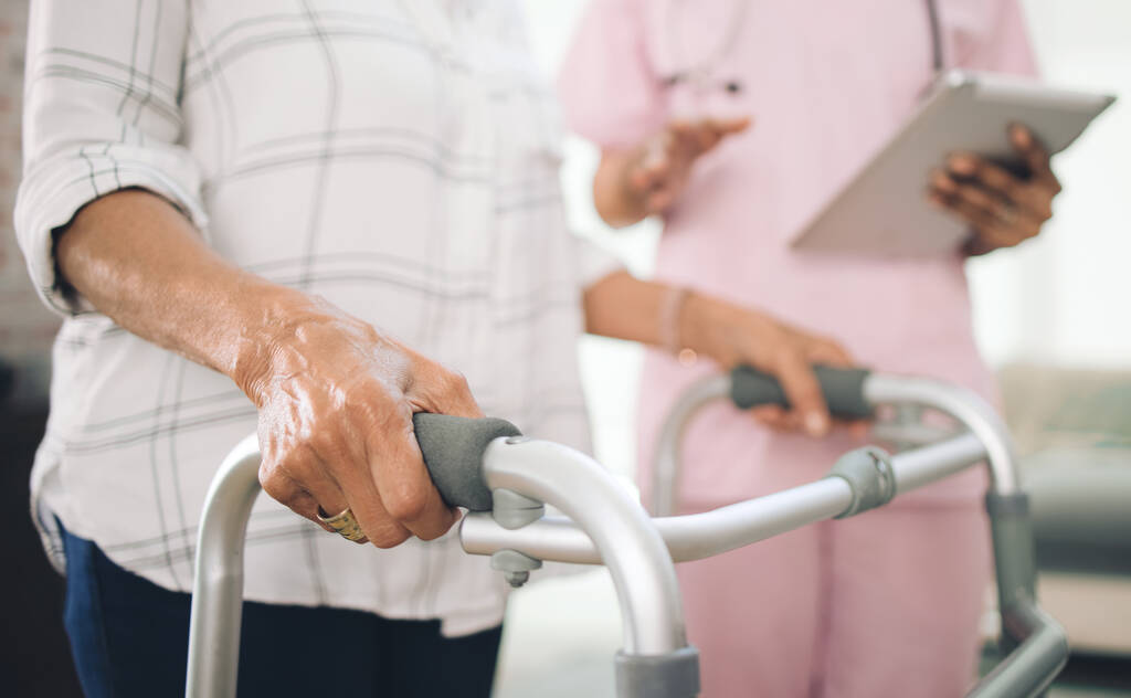 older woman using a walker and walking with the assistance of a physiotherapist